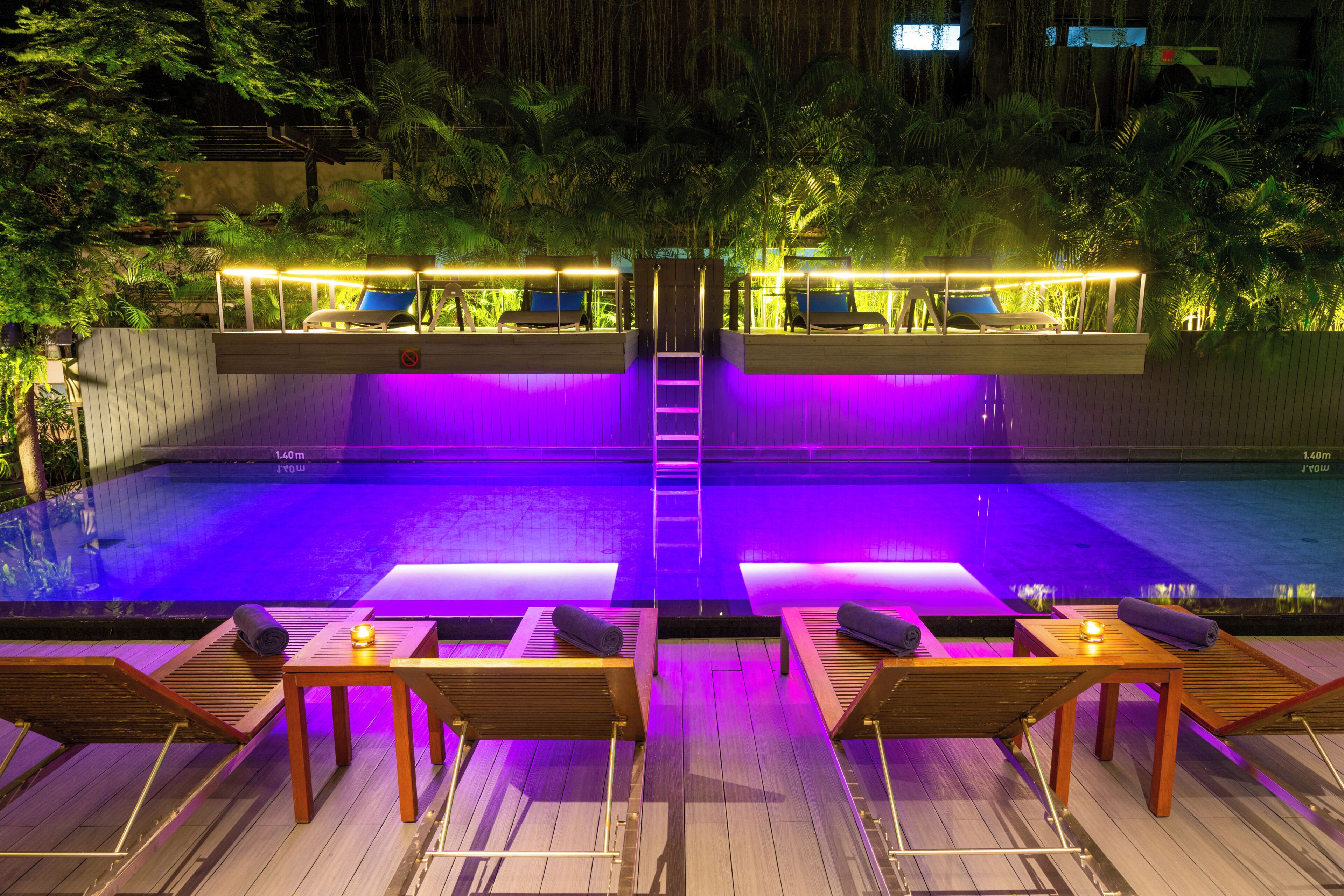 Piscina com deck de madeira, cadeiras de descanso e escada para área coberta.