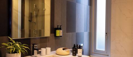 A modern bathroom with a large mirror, a sink, a potted plant, and toiletries on the counter.