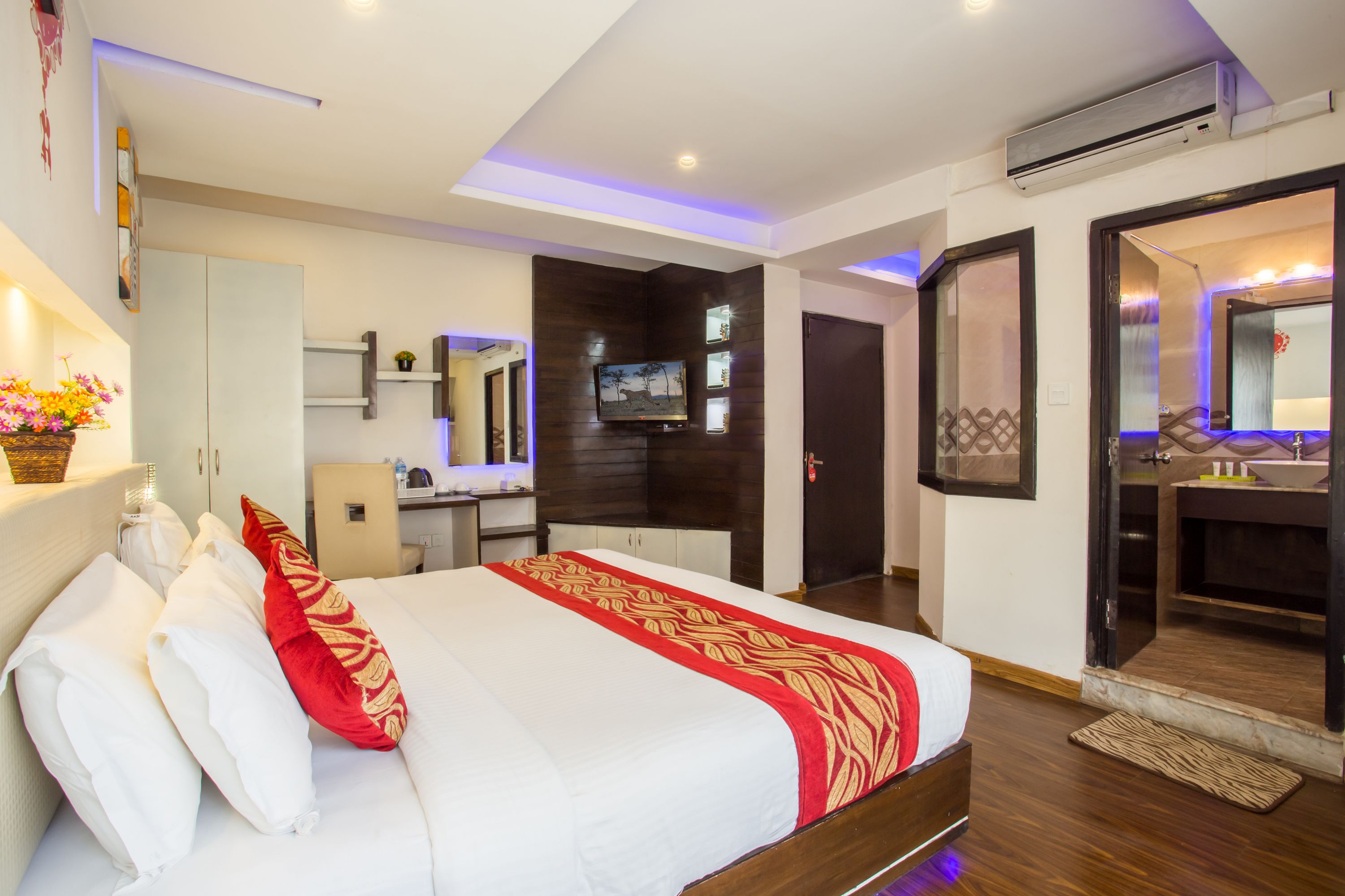 A hotel room with a bed, a desk, a TV, and a bathroom with a mirror and sink.