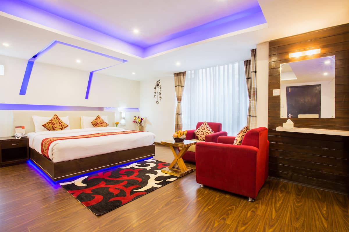 A modern hotel room with a large bed, red armchair, wooden floor, and a ceiling with blue lighting.