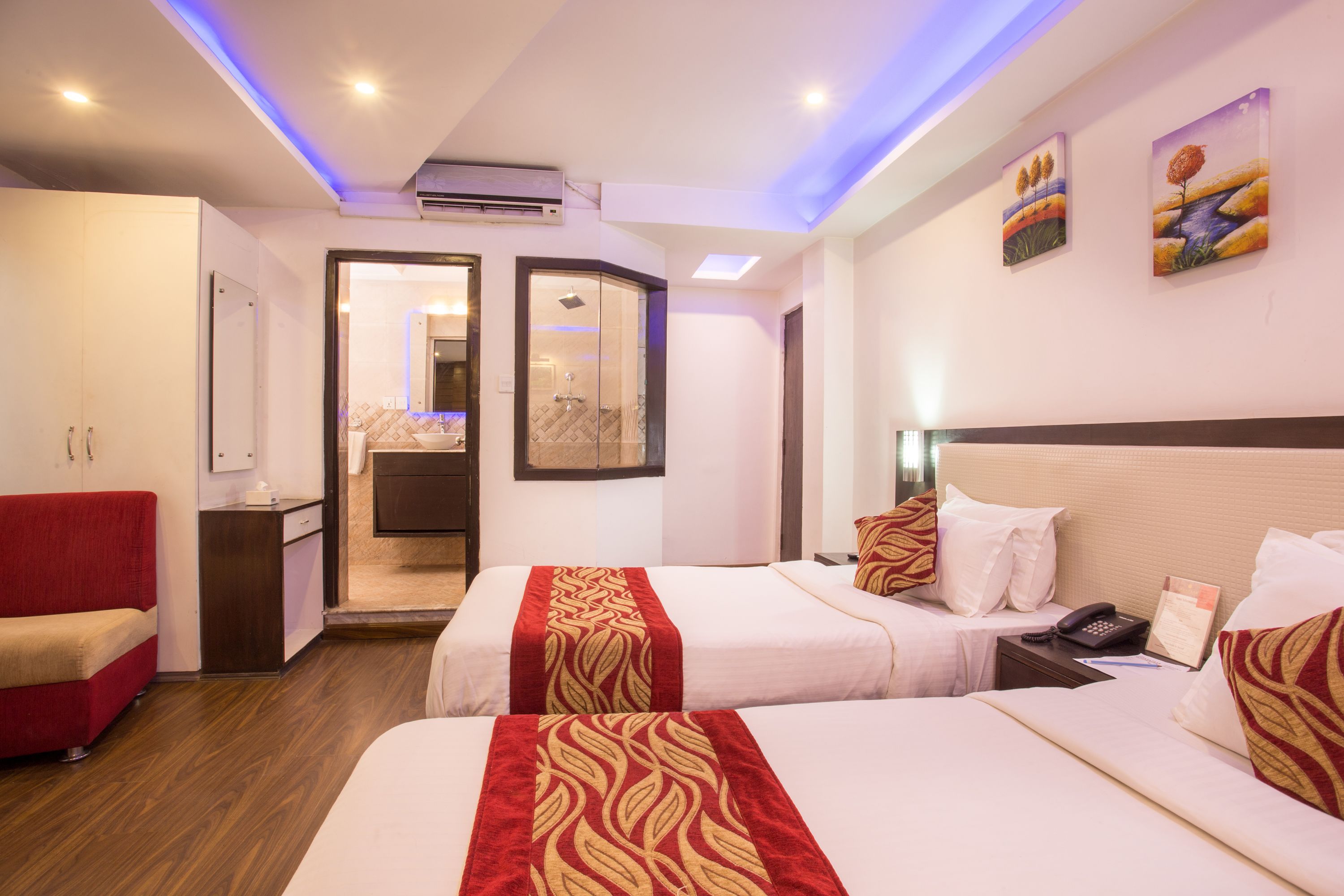 A hotel room with two beds, a red sofa, a shower area, and artwork on the walls.