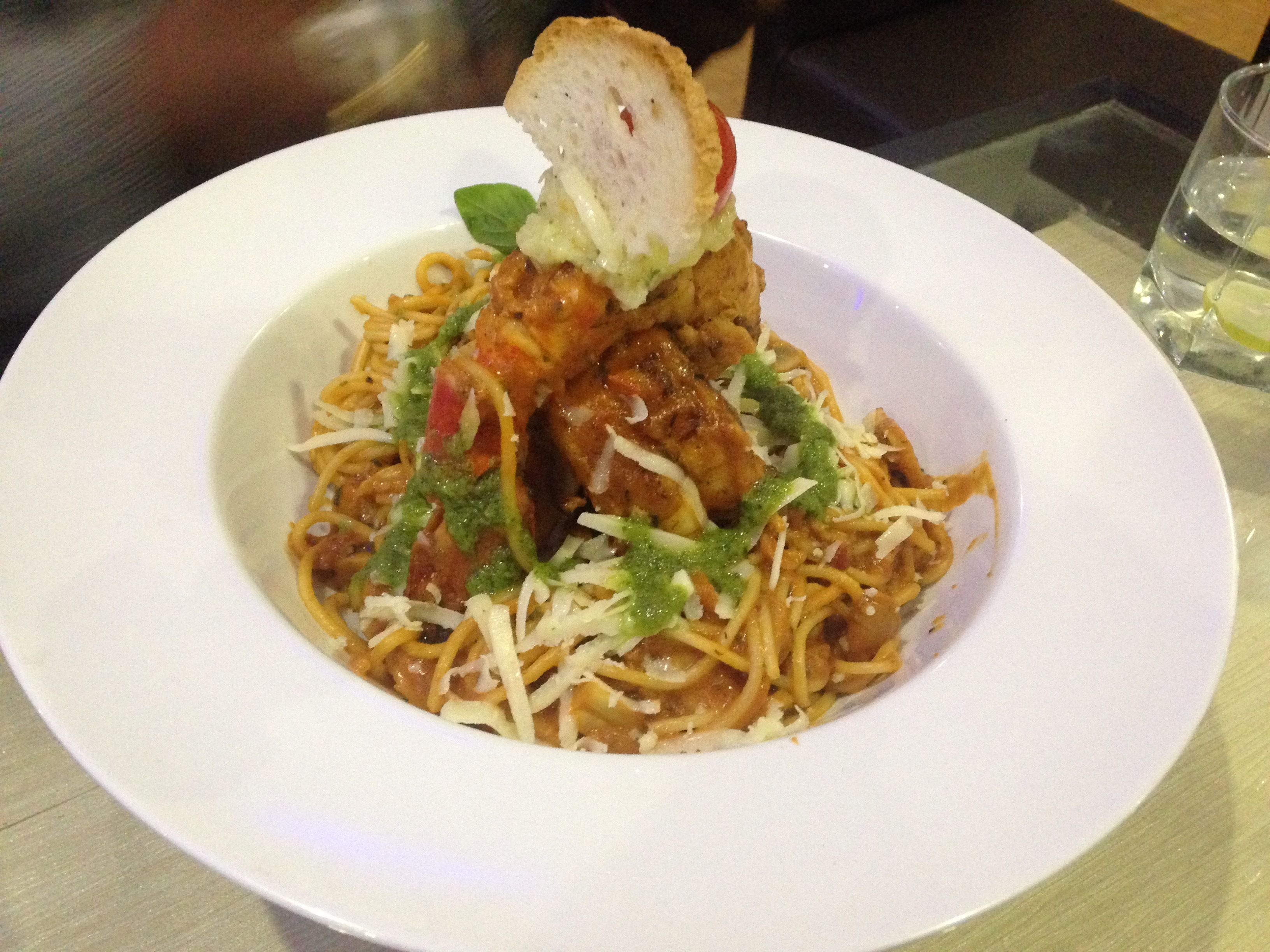 A plate of spaghetti with meatballs, topped with a slice of bread and a basil leaf.