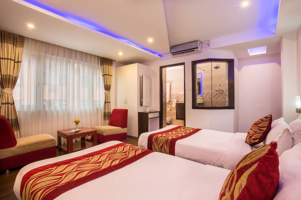 A hotel room with two beds, a sitting area with a red armchair, a small table, and a mirror.