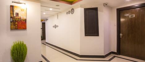 A hotel corridor with a potted plant, a wooden door with a number, and a wall with circular decorations.