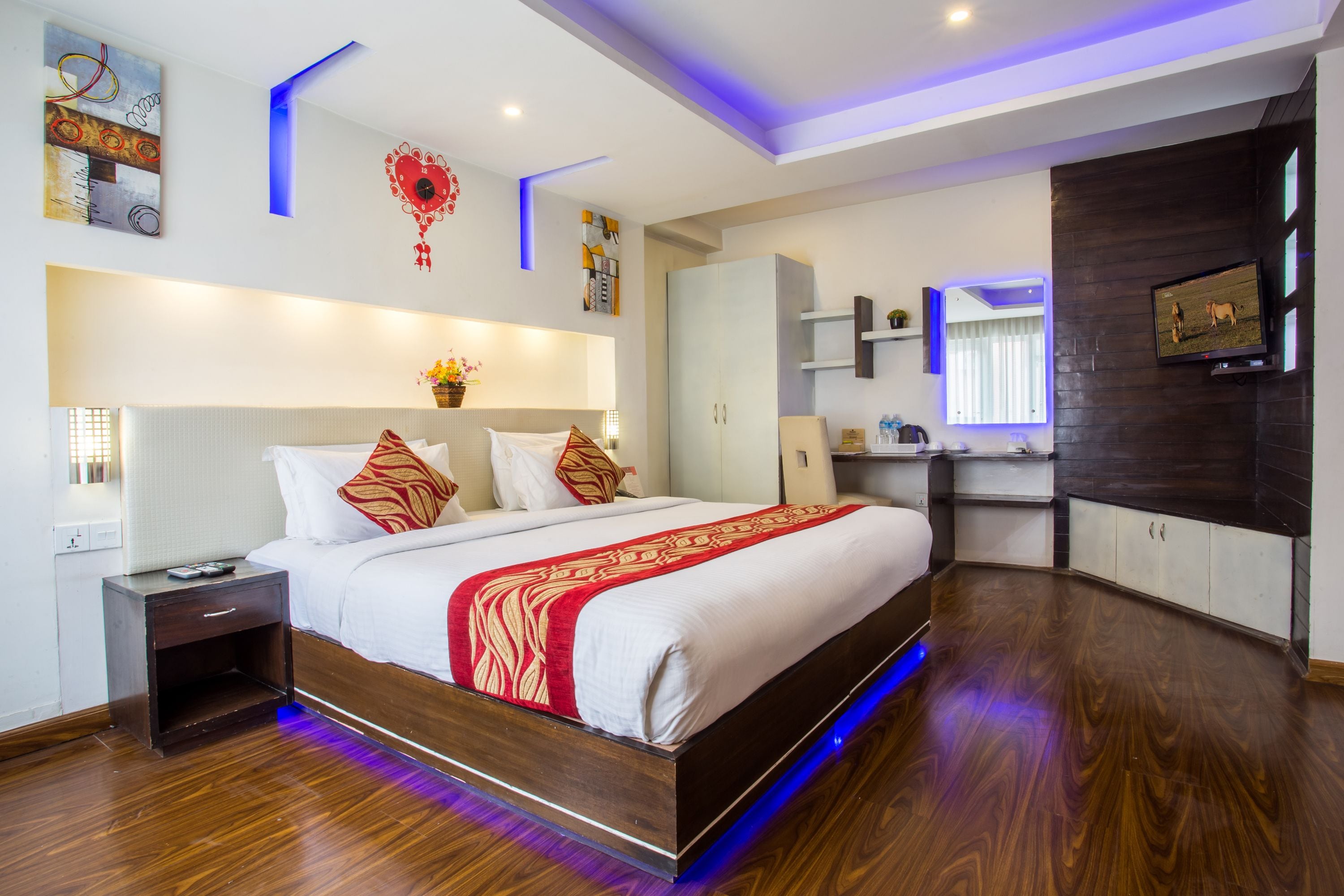 A modern bedroom with a large bed, bedside tables, a nightstand, a vanity with a mirror, and a television on the wall.
