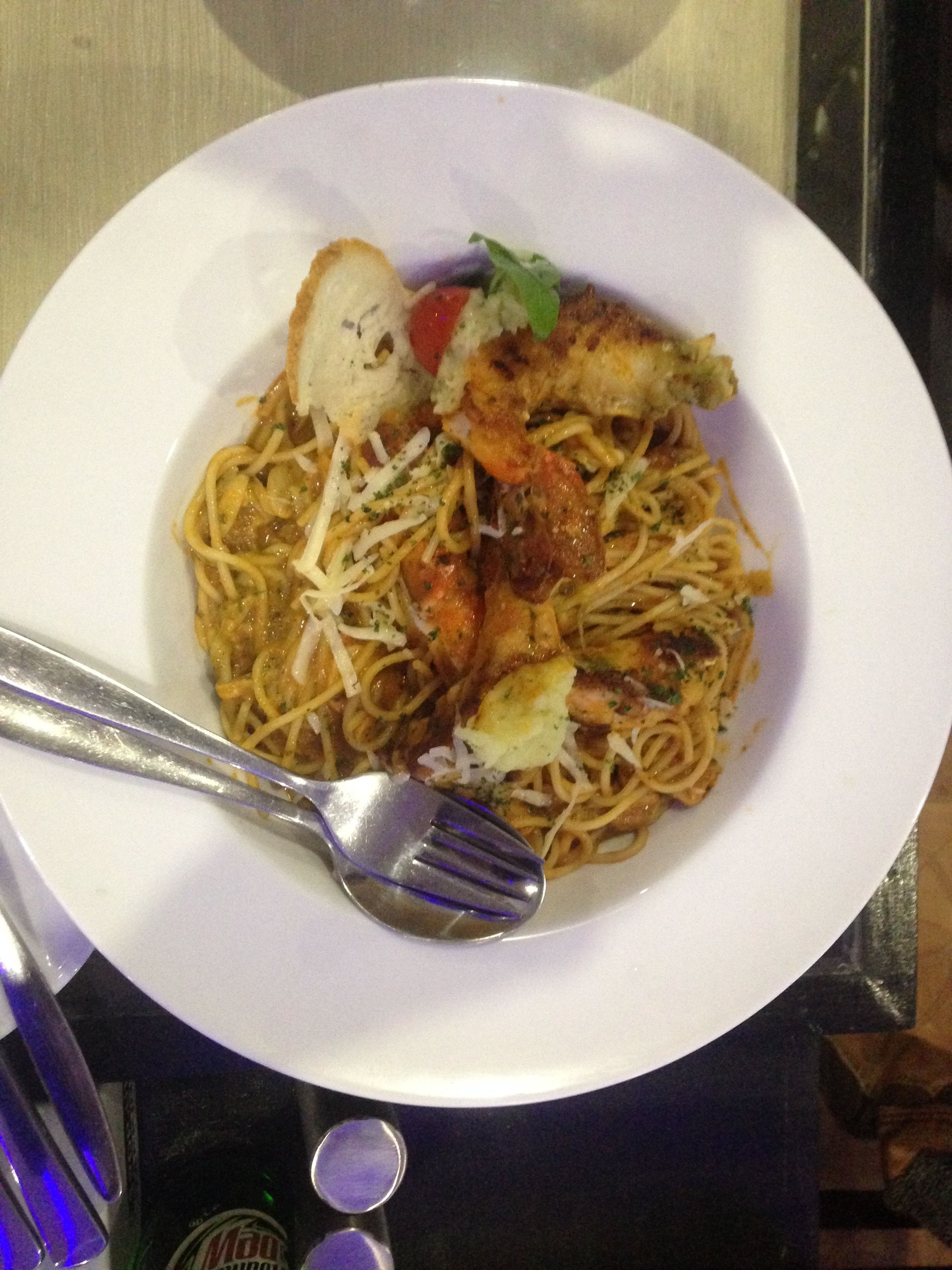 A plate of spaghetti with shrimp, cheese, and a slice of bread on a white plate.