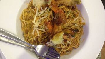 A plate of spaghetti with shrimp, cheese, and a slice of bread on a white plate.