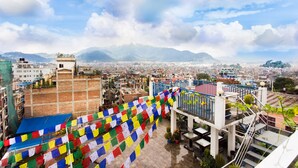 A cityscape with a view of mountains in the distance, a blue sky, and colorful prayer flags. - Avataar Kathmandu Hotel (Kathmandu)