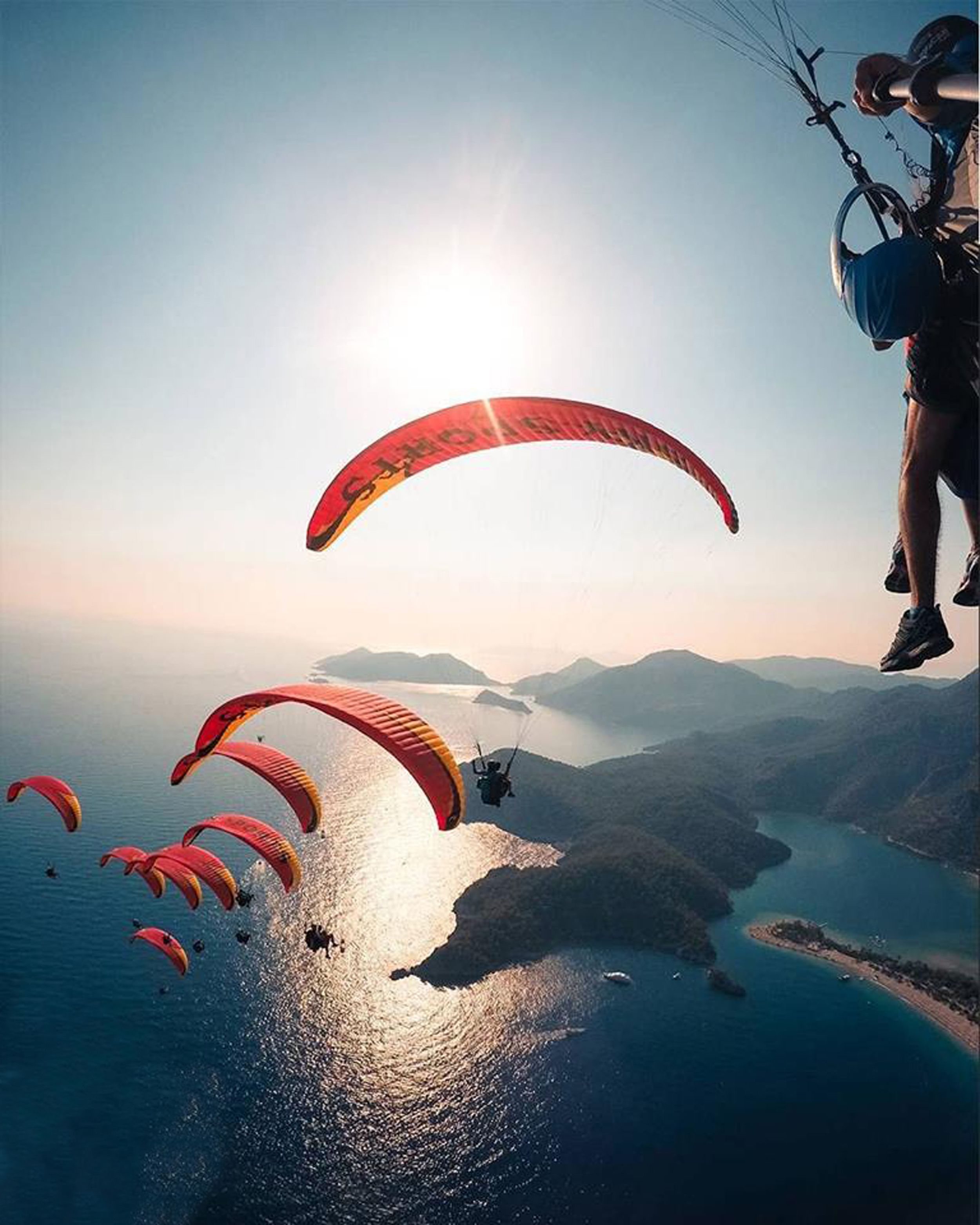 A person paragliding over a body of water with mountains in the background.