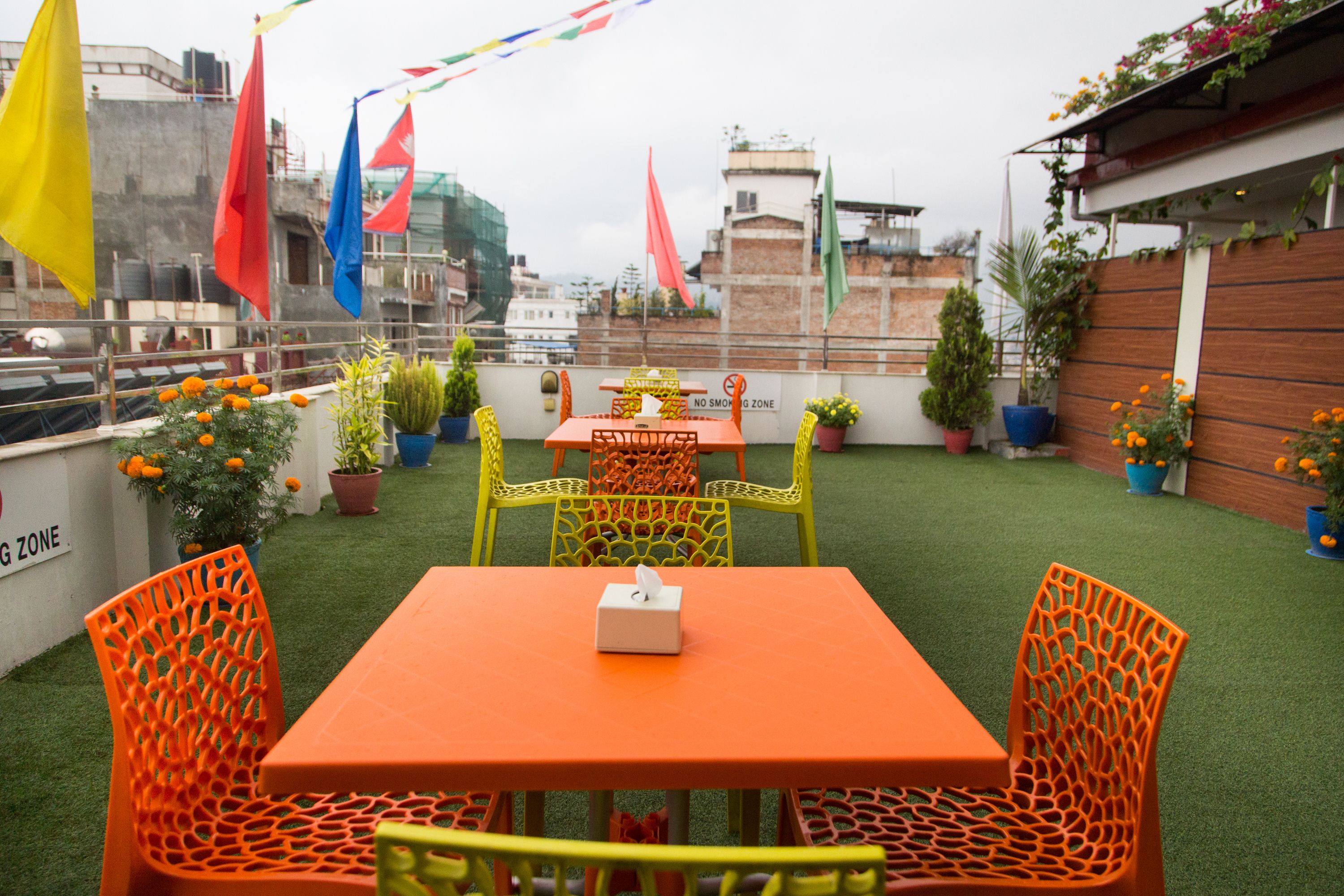 An outdoor seating area with a table and chairs, surrounded by potted plants and flags.
