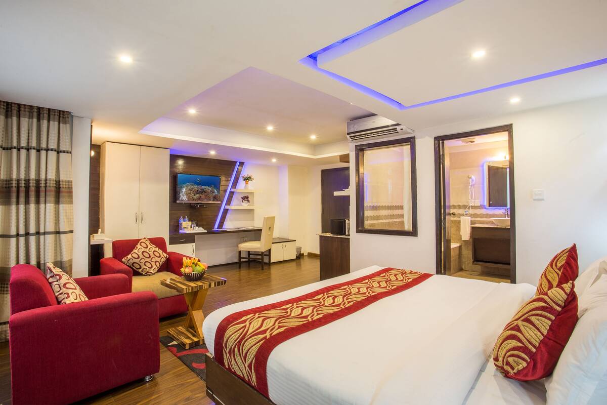 A modern hotel room with a large bed, a red sofa, a desk, and a bathroom visible through an open door.