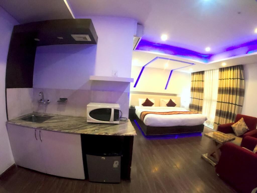 Habitación de hotel pequeña con kitchenette, una cama con cabecera, un sofá rojo y una ventana con cortinas.