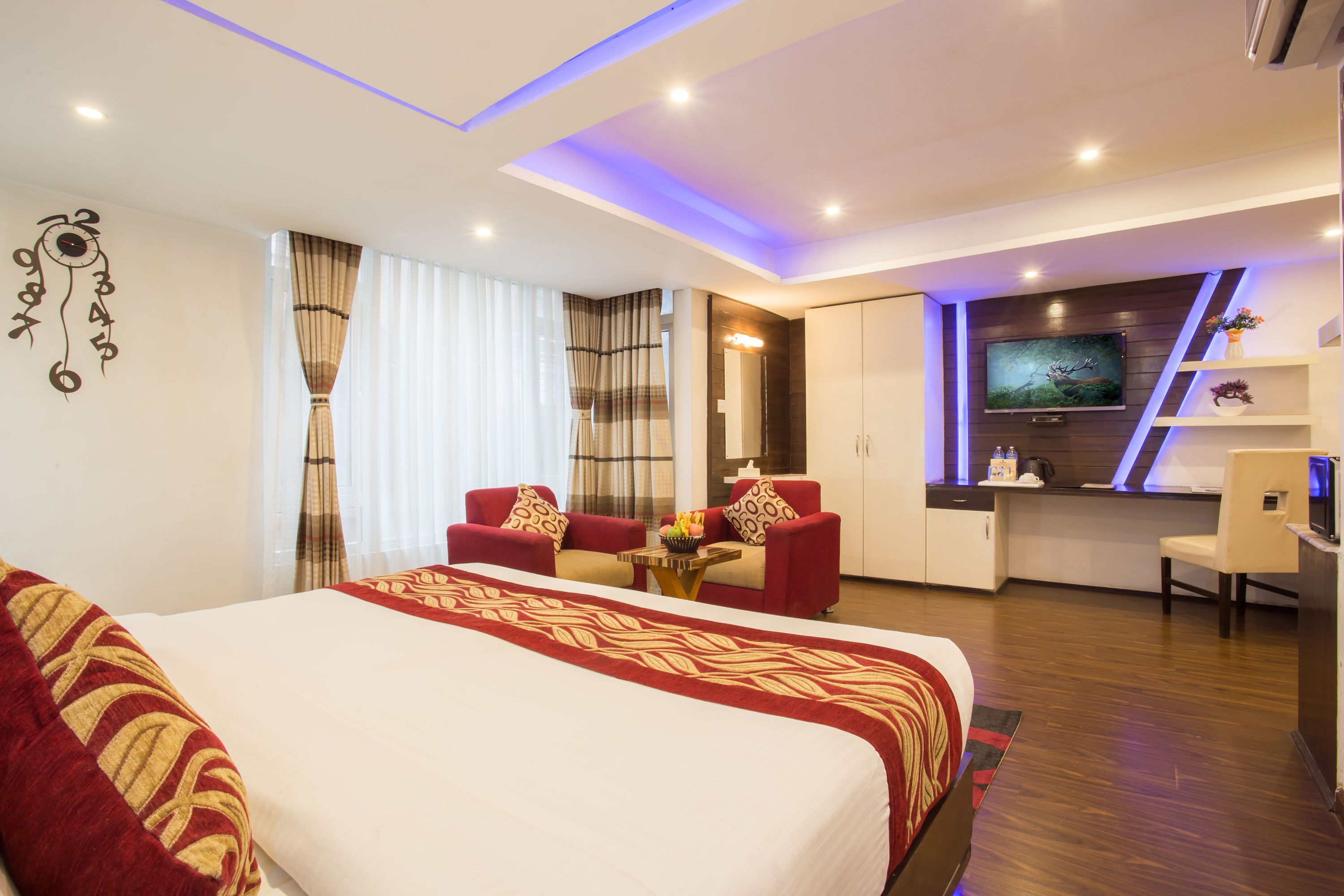 Ein modernes Hotelzimmer mit einem großen Bett, einem Schreibtisch, einem Fernseher und einer Sitzecke mit roten Stühlen.