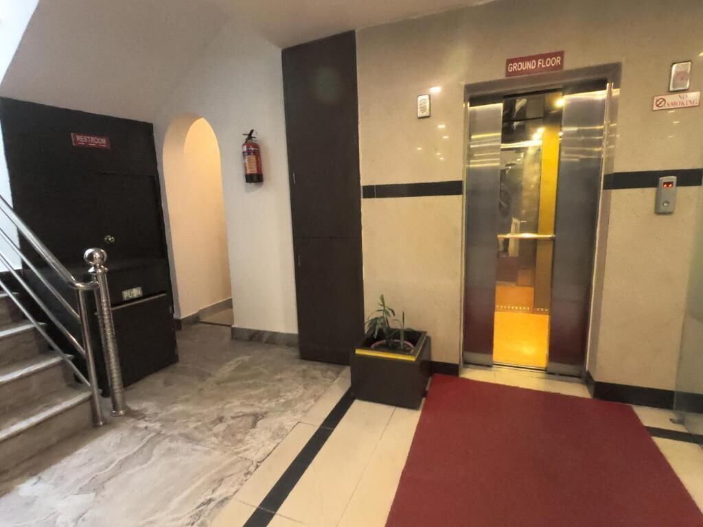 Un vestíbulo de hotel con una escalera, un baño, un extintor, un ascensor y una alfombra roja.