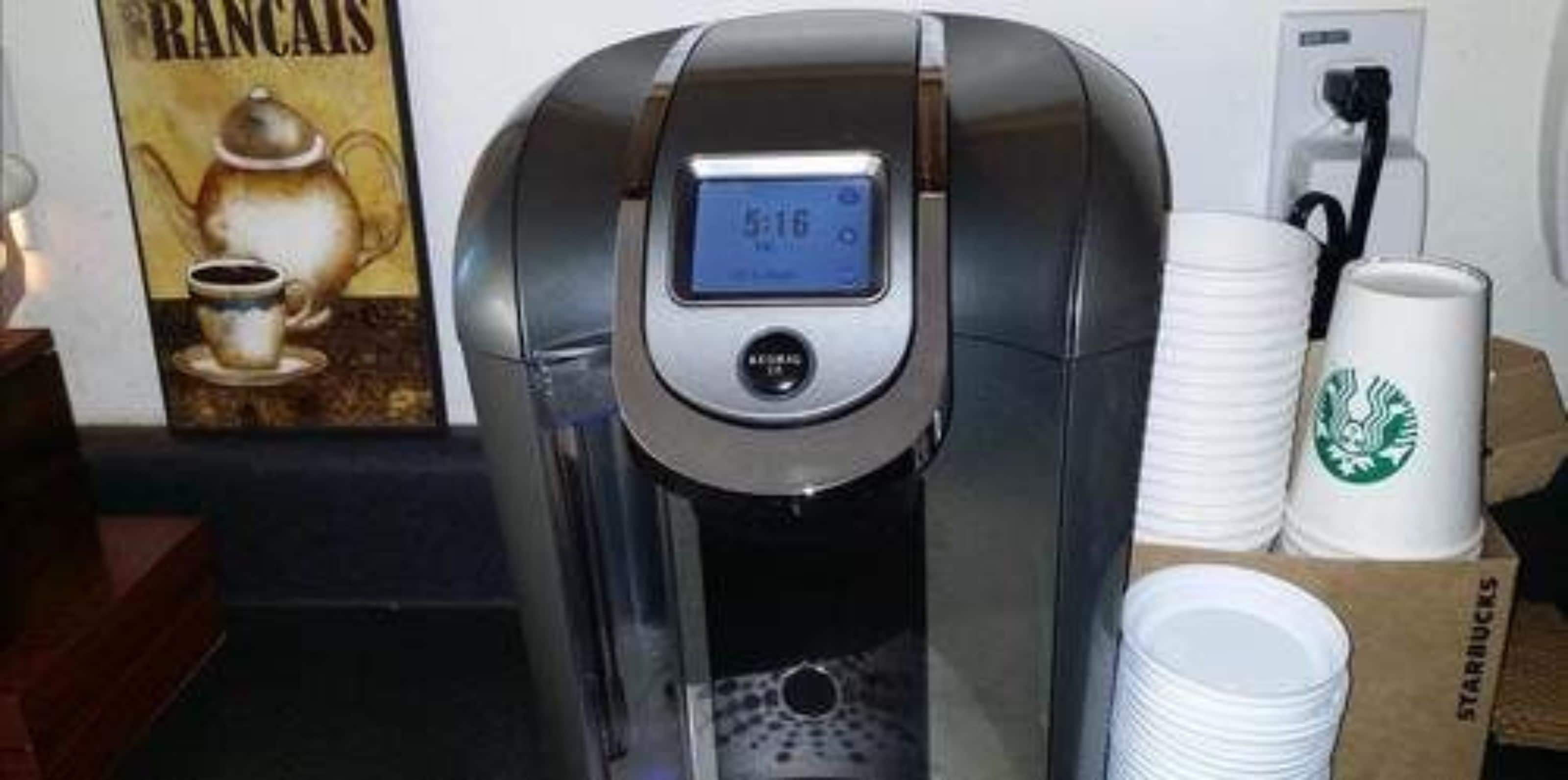 Eine Kaffeemaschine mit digitalem Display, eine Kaffeetasse sowie Starbucks-Tassen und -Deckel.