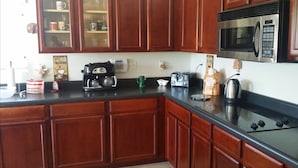 A kitchen with wooden cabinets, a black countertop, a coffee maker, a toaster, a kettle, and a microwave. - Happy Valley House (Phoenix)