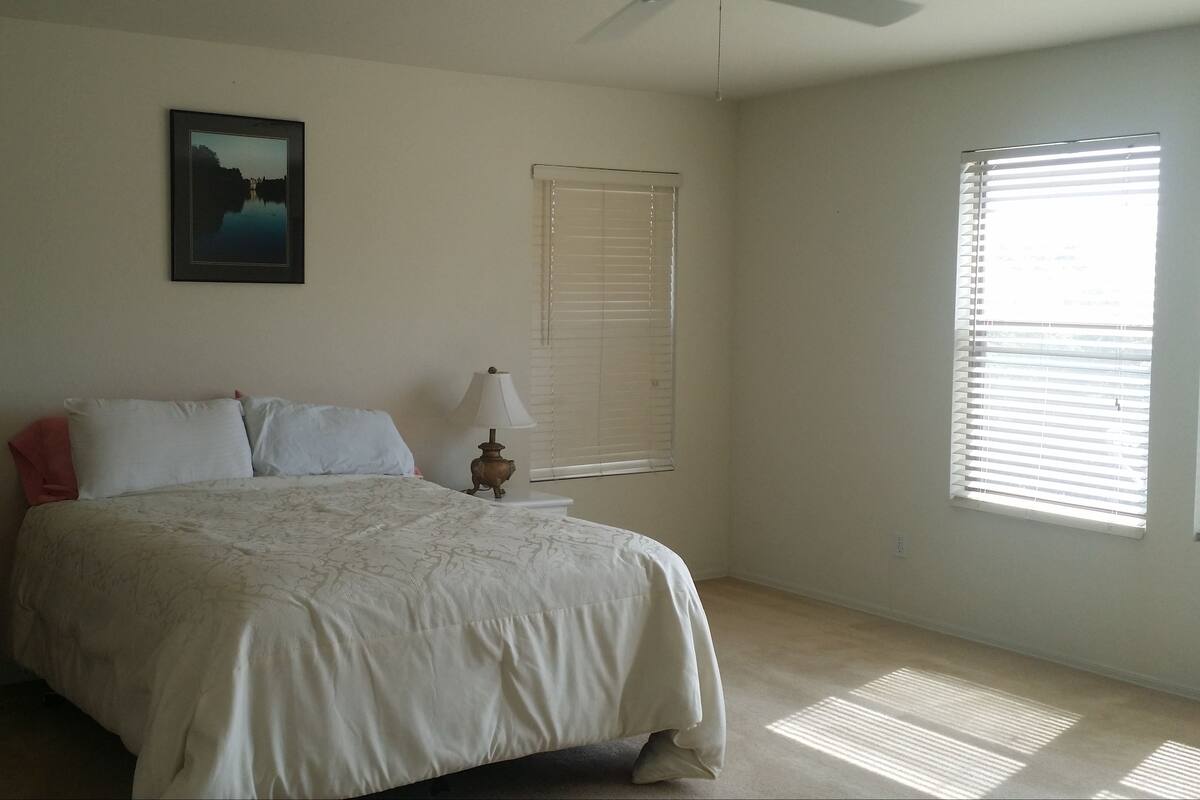 A bedroom with a bed, two bedside lamps, a picture on the wall, and a window with blinds.