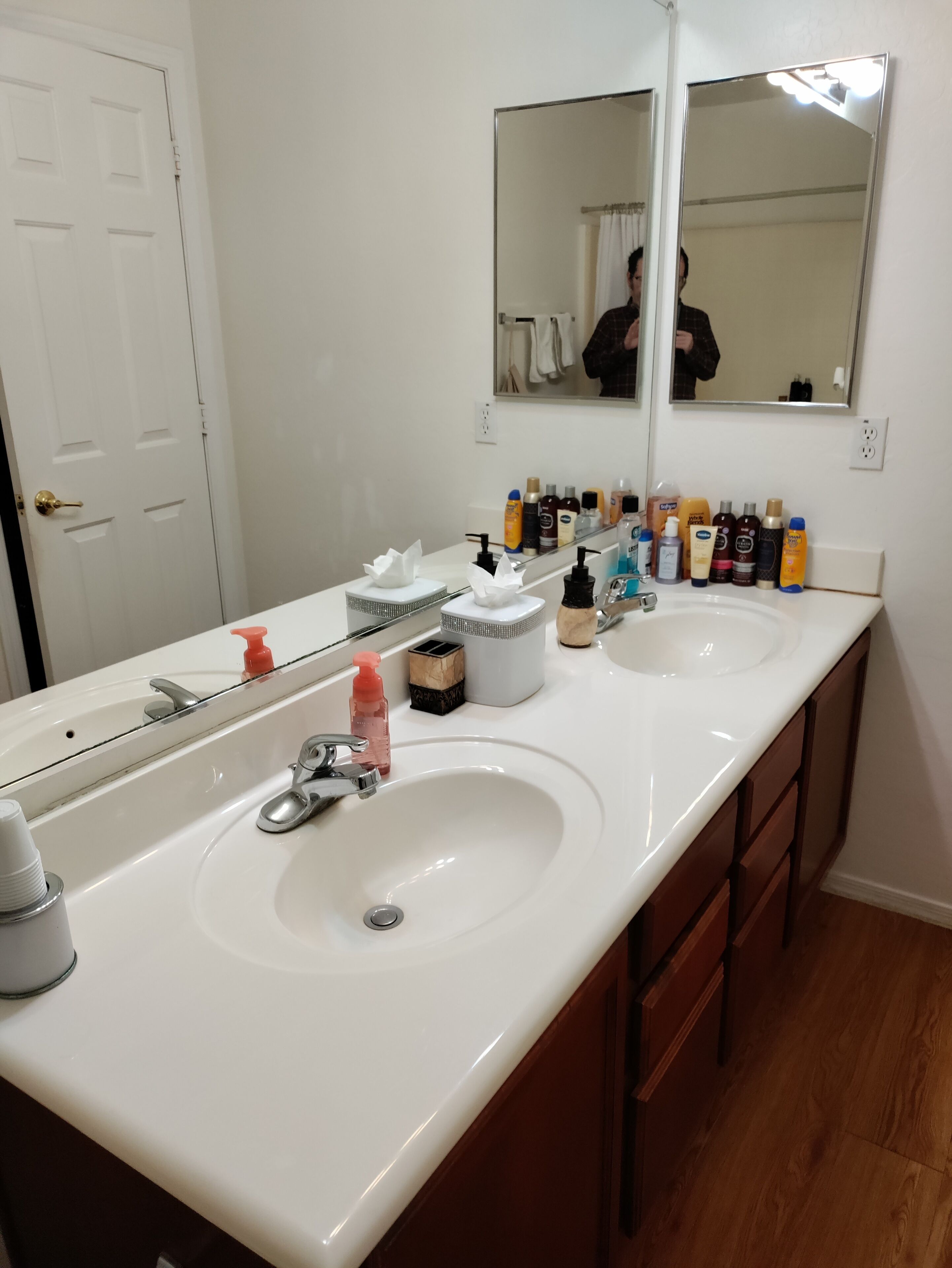 Une salle de bain avec un double vasque, un grand miroir et divers produits de toilette disposés sur le comptoir.