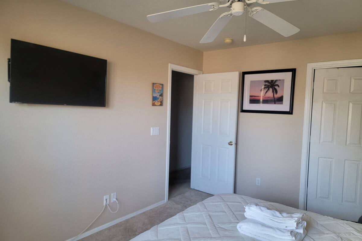 A bedroom with a bed, a ceiling fan, a TV, and a door leading to another room.