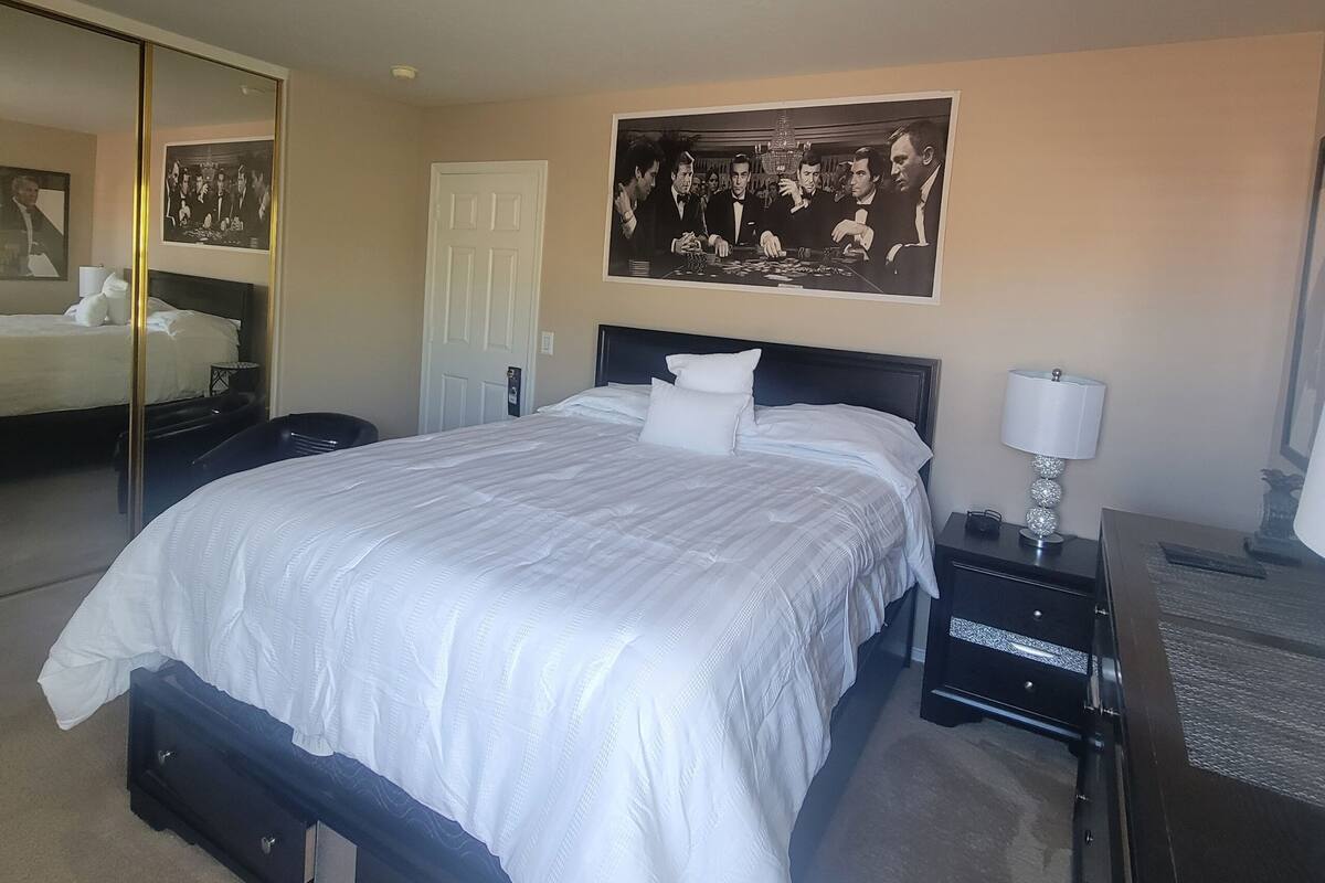 A hotel room with a large bed, a bedside table with a lamp, a mirror, and a framed picture on the wall.