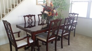 A dining table with six chairs, a vase of flowers, and a staircase in the background. - Happy Valley House (Phoenix)