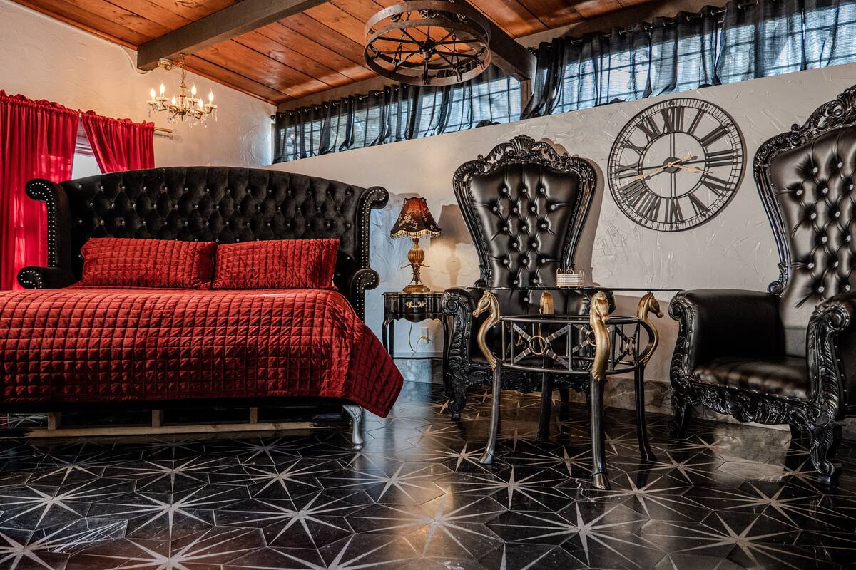 Een slaapkamer met een groot bed, twee sierlijke stoelen, een wandklok en een kroonluchter.