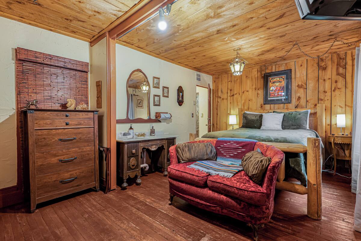 Een kamer met houten lambrisering, een bed, een rode bank, een dressoir en een spiegel.