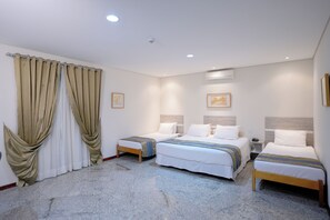 Een hotelkamer met twee enkele bedden, een groot raam met beige gordijnen en een marmeren vloer.