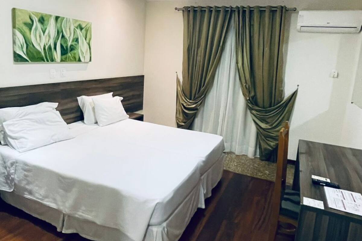 Une chambre d’hôtel avec un lit, un bureau, un appareil de climatisation et un tableau au mur.