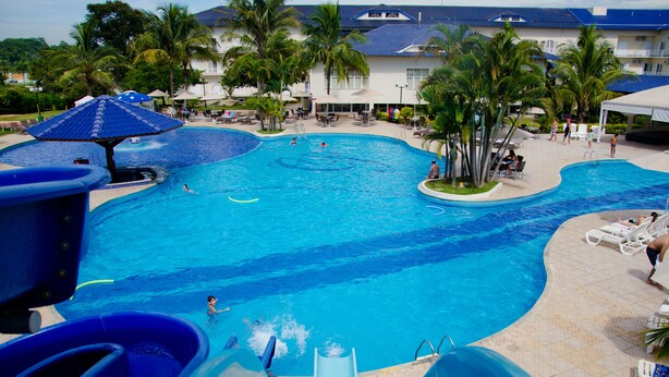 Una gran piscina al aire libre con un tobogán de agua, rodeada de palmeras y tumbonas.