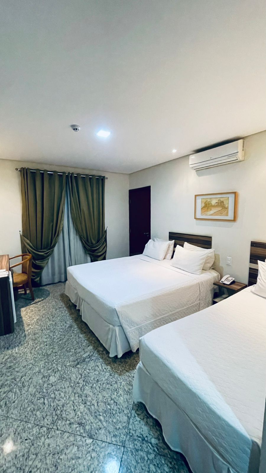 Habitación de hotel con dos camas, un escritorio, una silla, aire acondicionado y un cuadro en la pared.