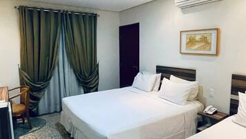Habitación de hotel con dos camas, un escritorio, una silla, aire acondicionado y un cuadro en la pared.