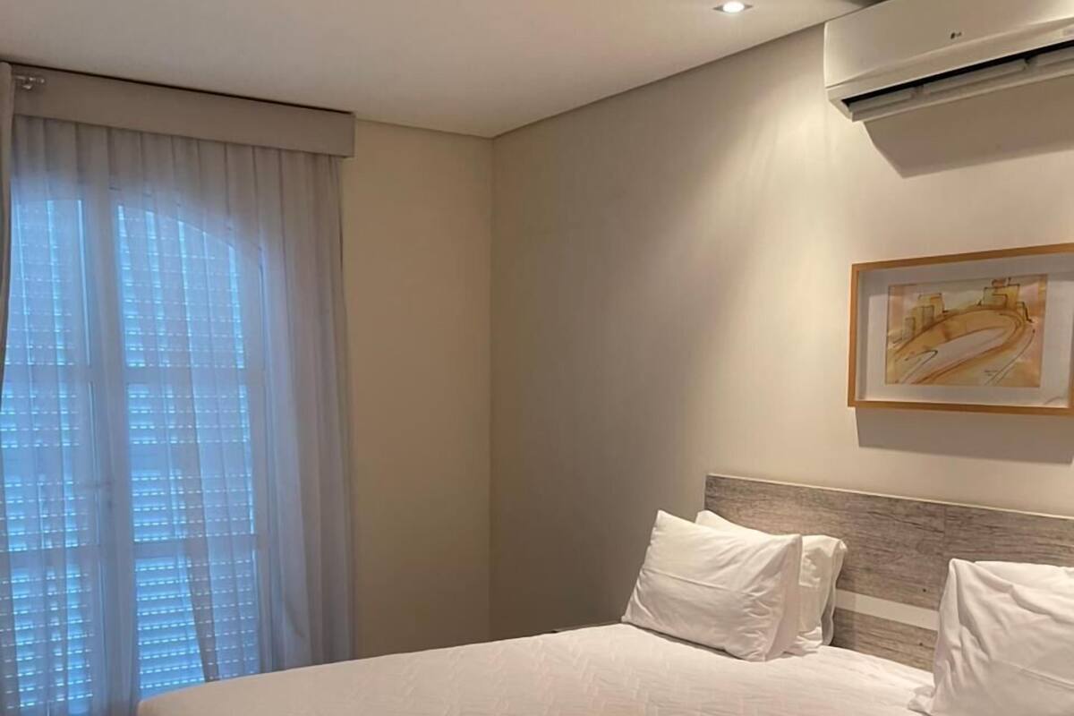 Une chambre d’hôtel avec un grand lit, un climatiseur fixé au plafond et une fenêtre ornée de rideaux légers.