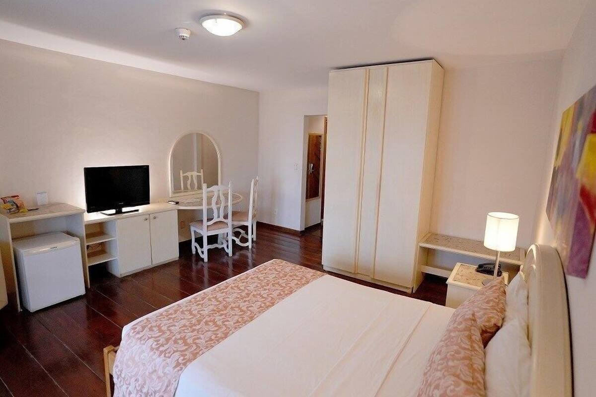 Une chambre d’hôtel comprenant un lit, un bureau avec une télévision, une armoire et une table de chevet avec une lampe.