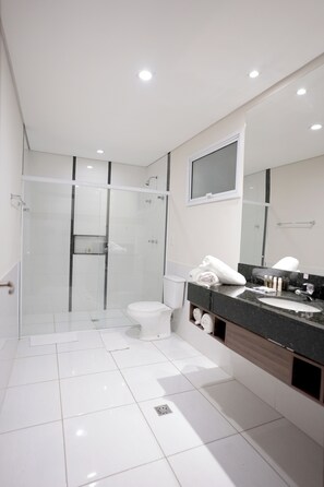 Een moderne badkamer met een glazen douchecabine, een wit toilet en een wastafel met spiegel en wasbak.