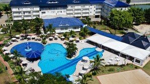 Un hotel con varias piscinas, cancha de tenis y un edificio grande de techo azul.