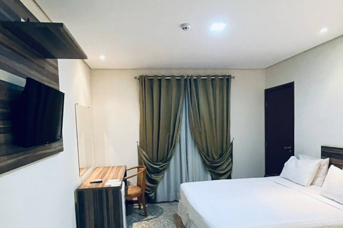 Une chambre d’hôtel avec un lit, un bureau, une chaise, une télévision et une fenêtre avec des rideaux.