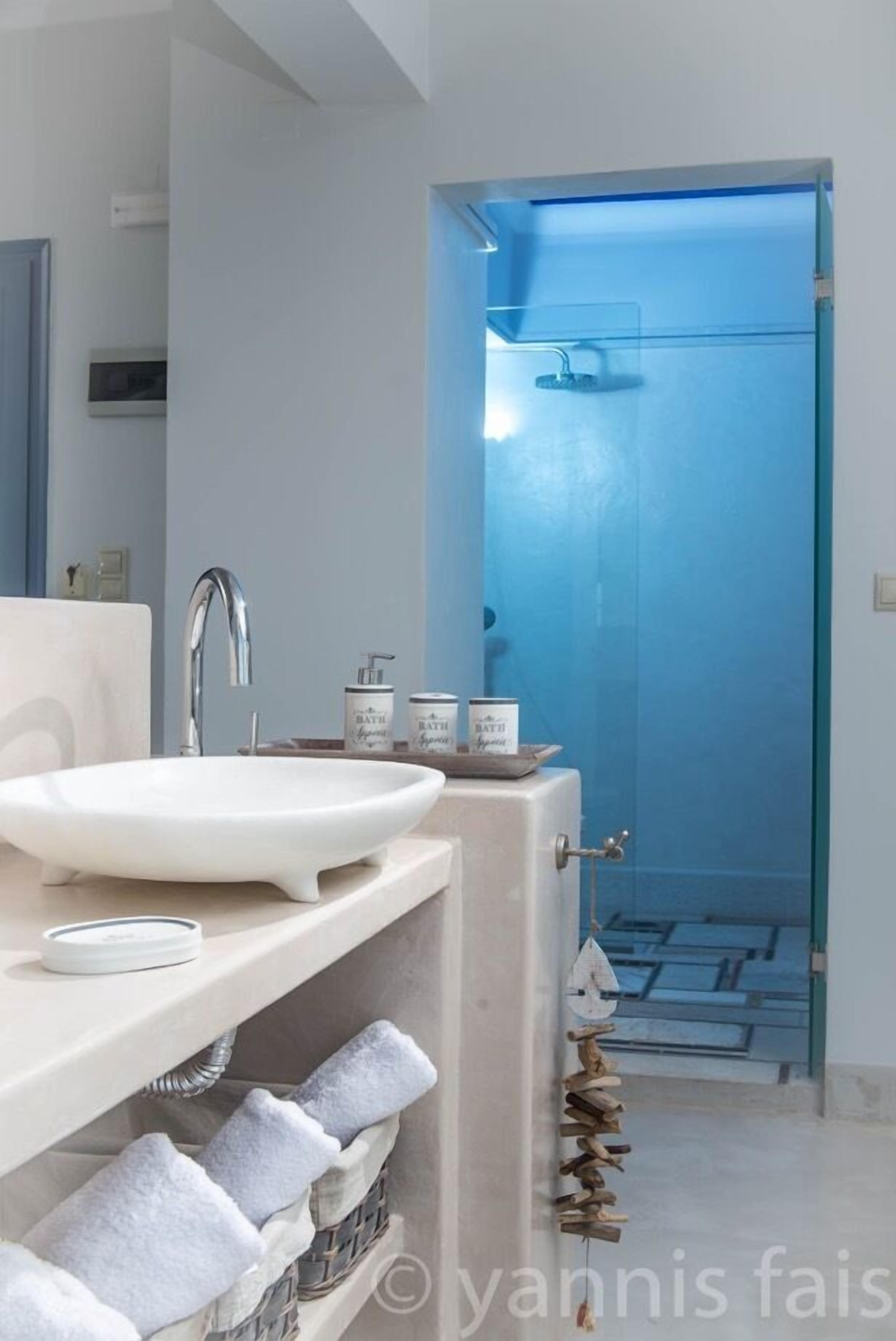 Un baño moderno con un lavabo blanco, una ducha con puerta de vidrio y un perchero con toallas dobladas.