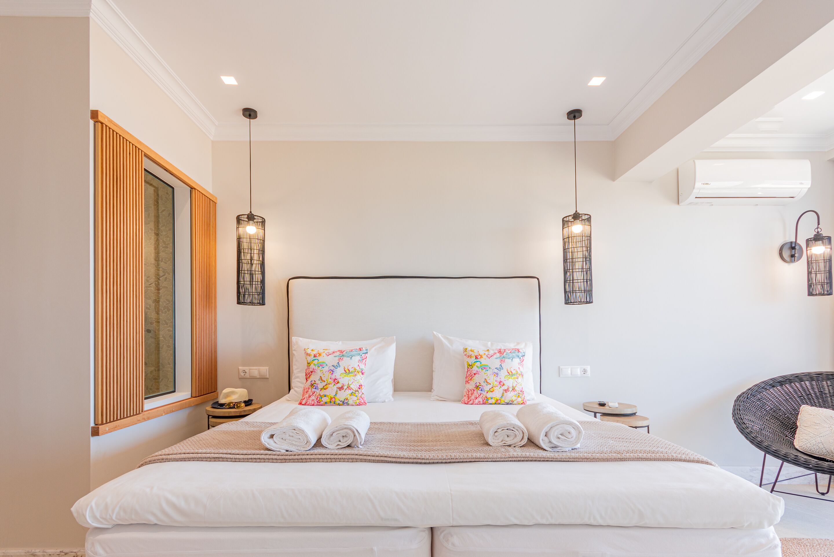 A neatly made bed with white linens, two decorative pillows, and rolled towels on a bedside table.