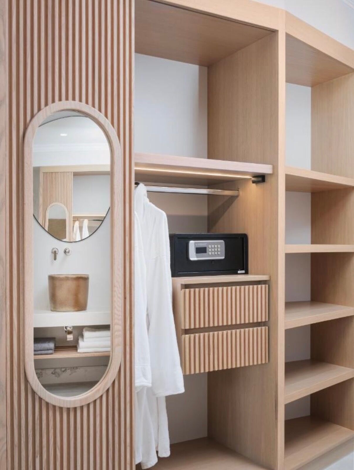 A modern bathroom with a wooden vanity, a round mirror, a sink, and a towel rack.