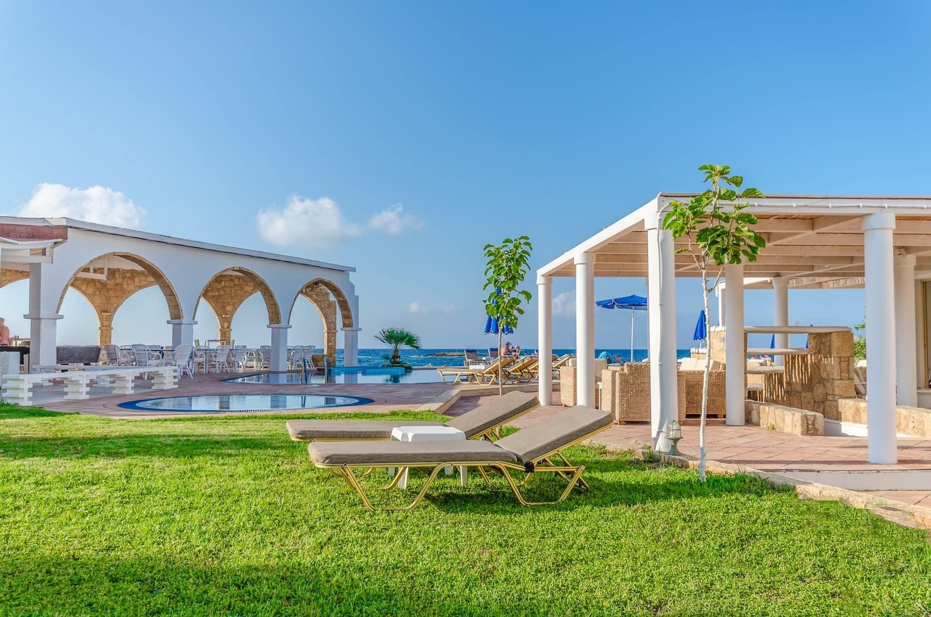 Un espace aménagé au bord de la piscine, avec des chaises longues, une piscine et un coin salon couvert équipé de parasols.