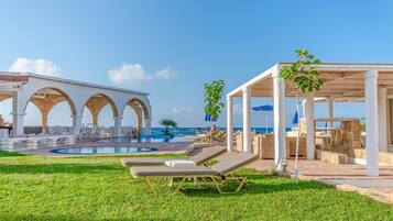 Un espace aménagé au bord de la piscine, avec des chaises longues, une piscine et un coin salon couvert équipé de parasols.