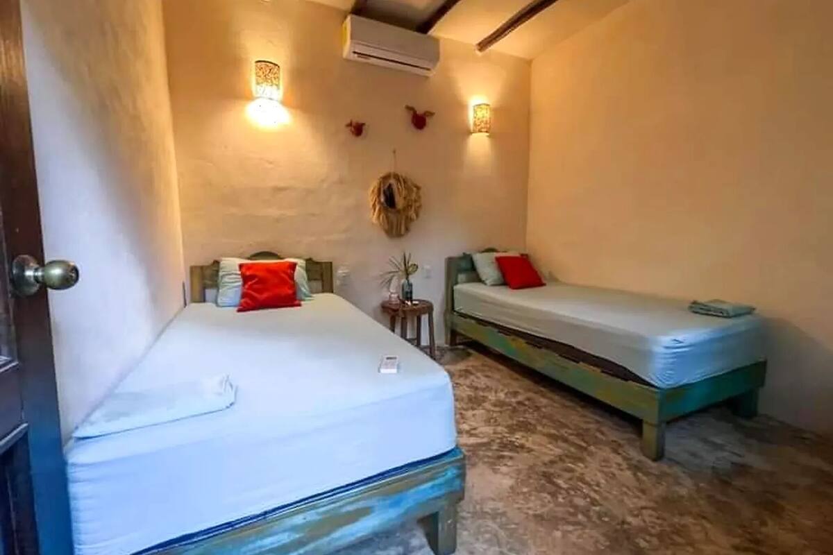 Una habitación pequeña y acogedora con dos camas, aire acondicionado de pared y dos apliques.