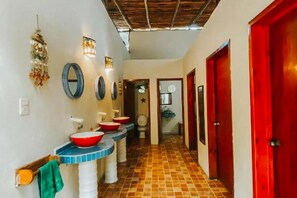 A hallway with a tiled floor, a row of sinks with red bowls, and a red door at the end. - Tubo Tulum Hostel - Unique Stay (Tulum)