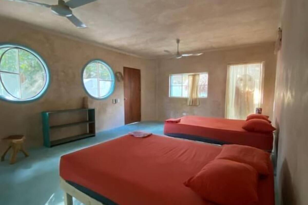 Una habitación con dos camas, un ventilador de techo, un taburete pequeño y una ventana.