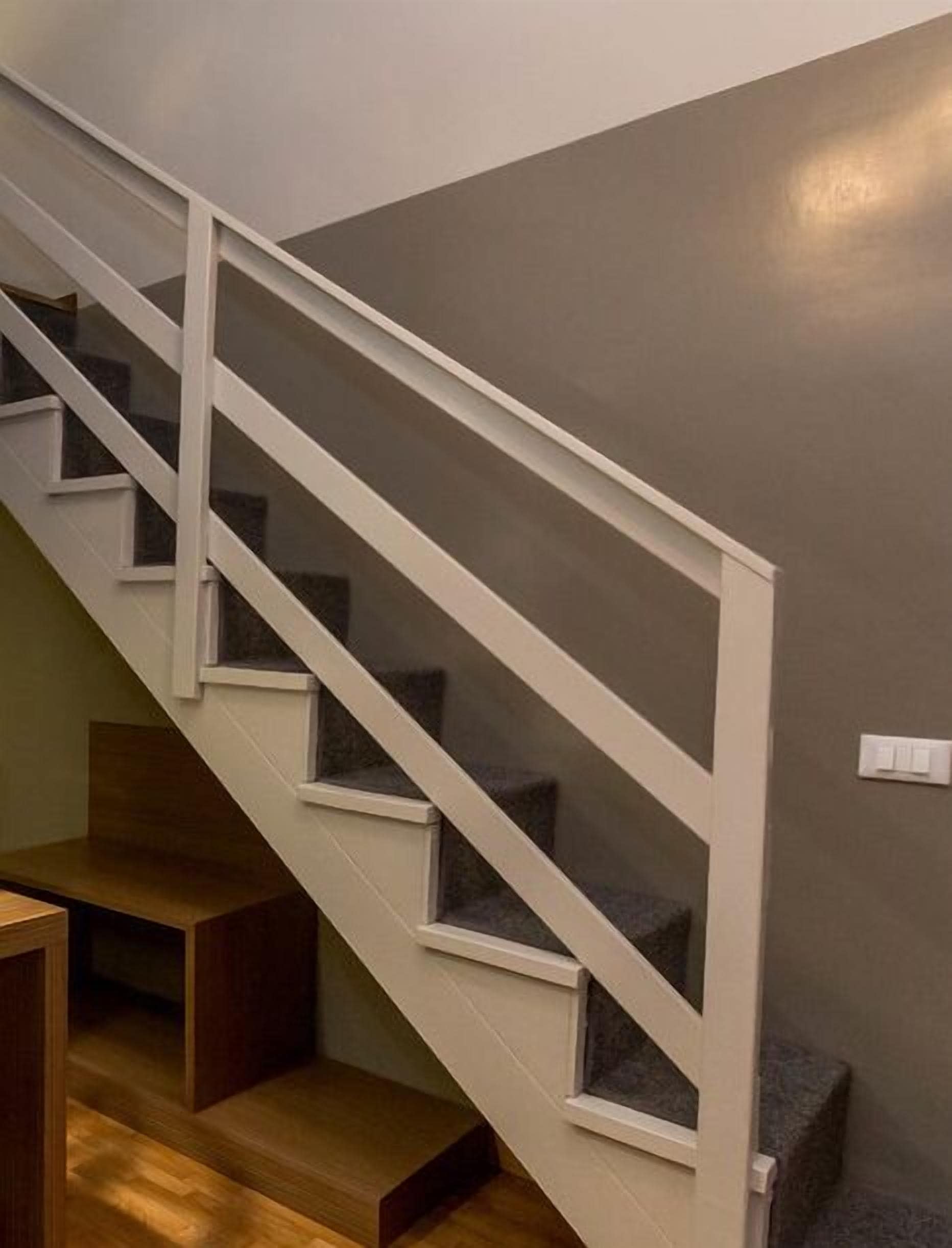 A staircase with white railings and dark steps, leading to a landing with a light switch.