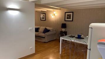 Un espacio habitable compacto con kitchenette, una zona de comedor con mesa y sillas, y un sofá al fondo.