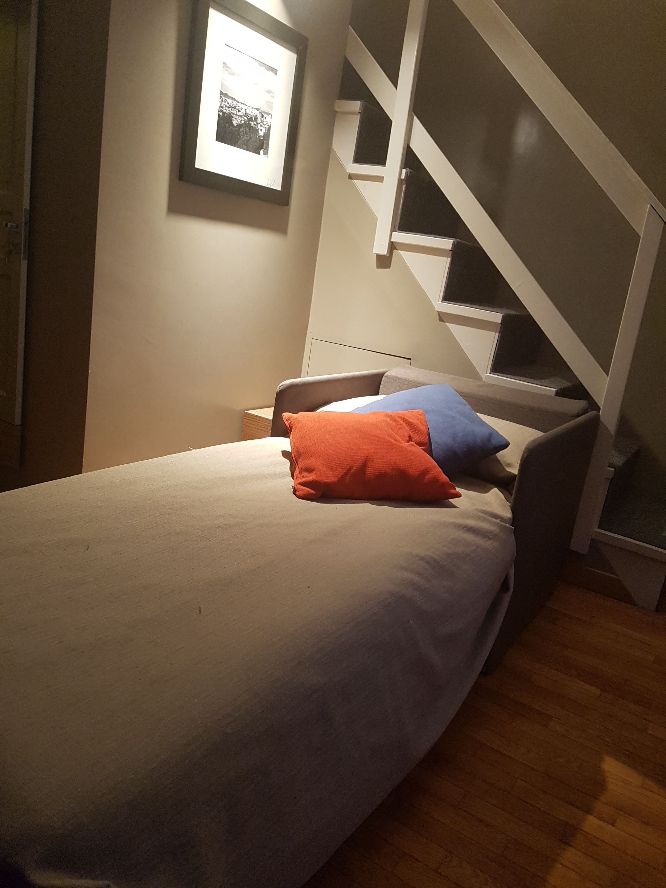 Ein Schlafzimmer mit einem Bett, einem Nachttisch, einem gerahmten Bild an der Wand und einer Treppe.