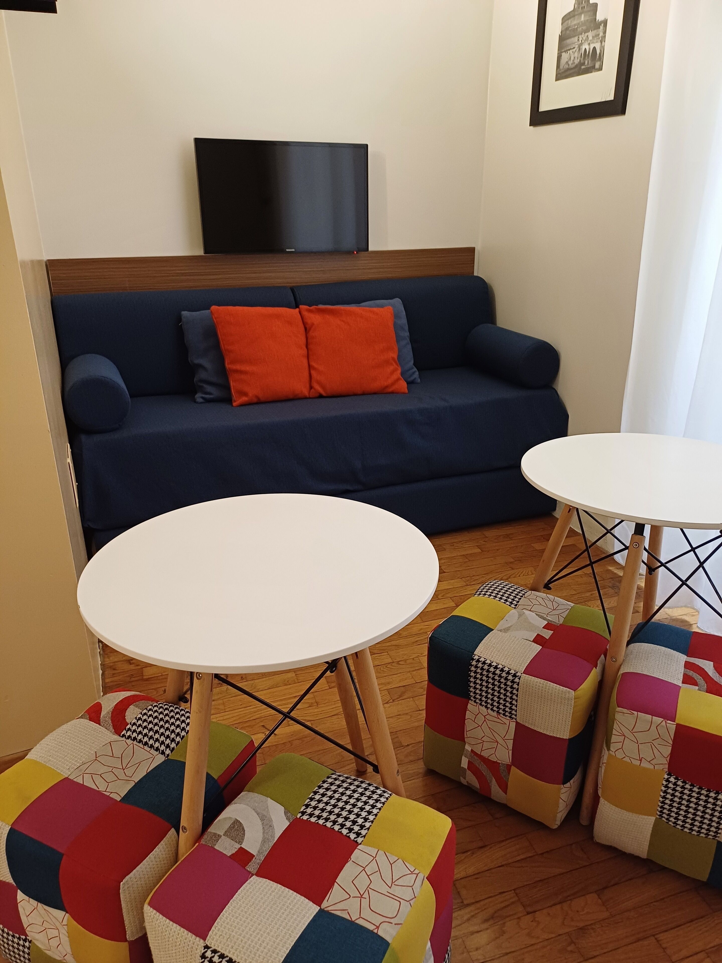 Un salón con un sofá azul, dos mesitas redondas blancas y otomanas de patchwork colorido.