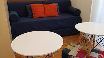 Un salón con un sofá azul, dos mesitas redondas blancas y otomanas de patchwork colorido.